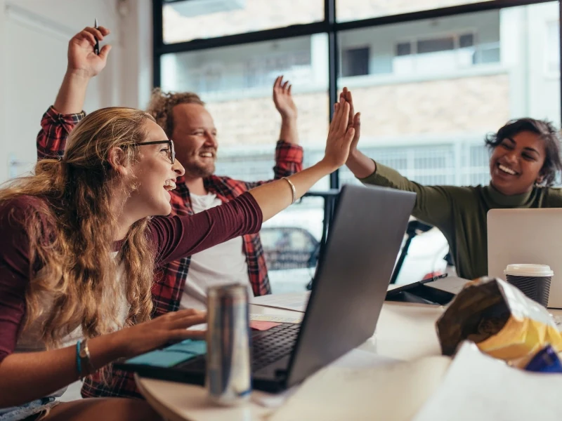 A team celebrating with high-fives around their laptops during a quiz showdown